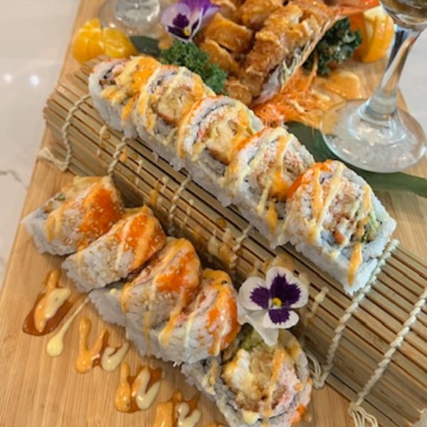 Two rows of sushi rolls with orange and white sauces, garnished with flowers on a wooden board.