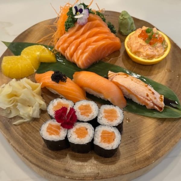 A wooden platter with salmon sashimi, nigiri, maki rolls, salmon salad, wasabi, and pickled ginger.